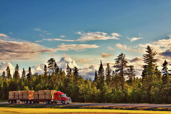 Under the big Canadian sky - a long red truck loaded with lumber and driving on a highway in New Brunswick, 